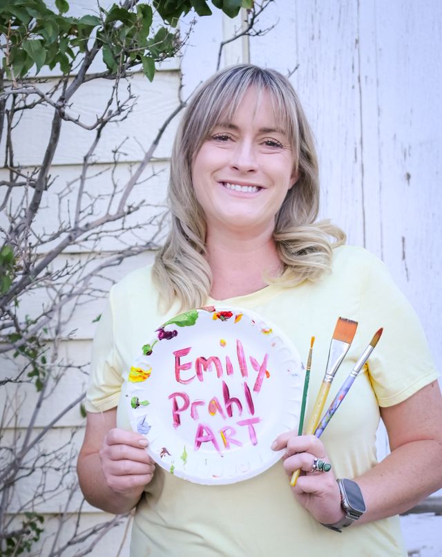 Emily Prahl smiling and holding a painted palette that reads Emily Prahl Art